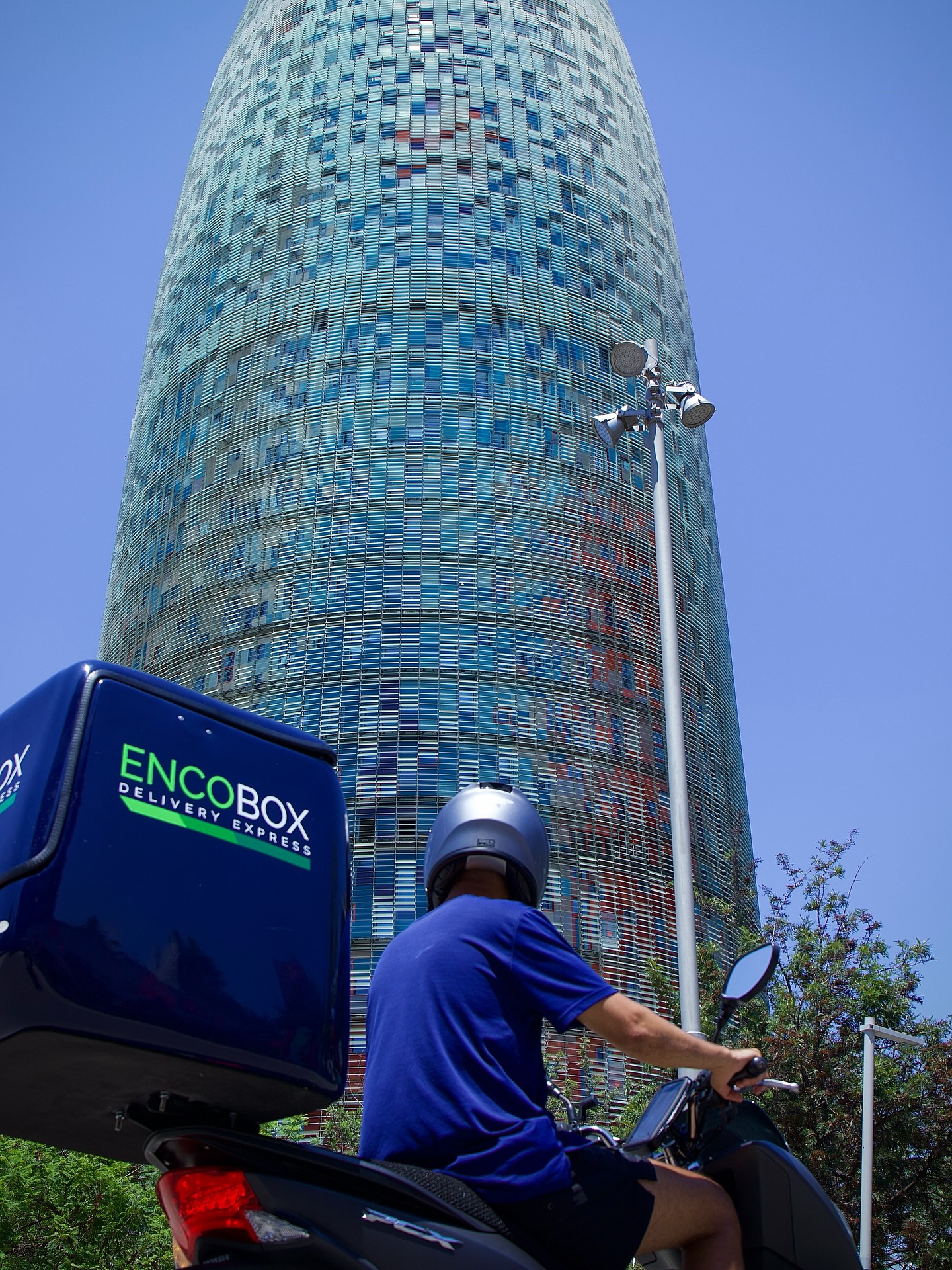 Repartidor Encobox en moto con la Torre Agbar de Barcelona al fondo